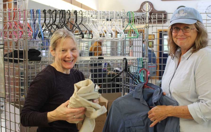 Two people smile at the camera while organizing clothing during a service project with Outward Bound. 